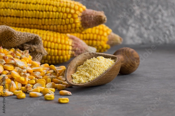 Fototapeta Corn flour in wooden bowl and spoon with dried corn groats, kernels on rustic table. corn ingredients concept