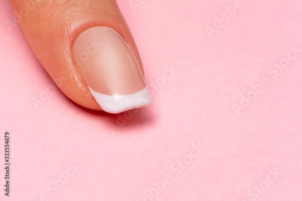 Obraz single female finger with a beautiful manicure on a pink background, close-up. clean healthy fingernails. copy space. place for text and logo.