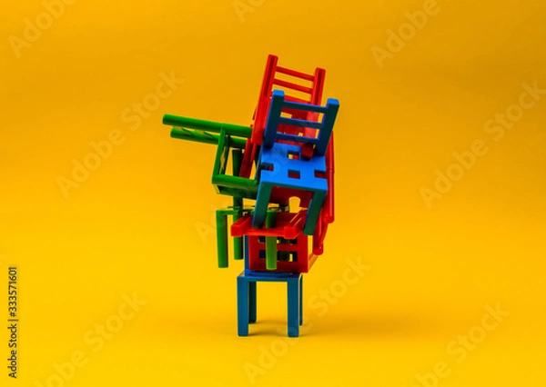 Obraz Plastic chairs stand on top of each other on a yellow background. The concept of solving complex problems, confusing situation, problems in business.