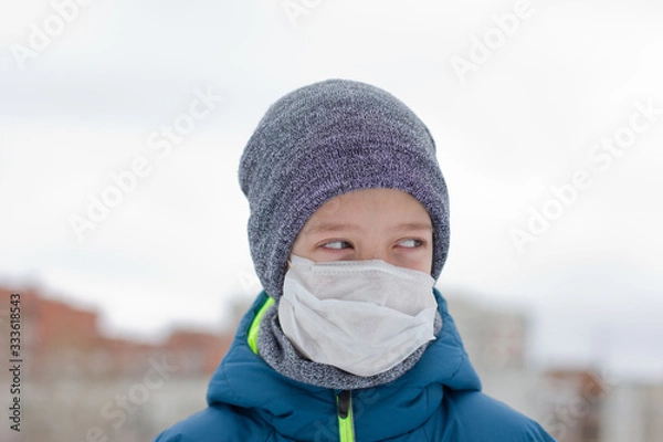 Fototapeta The danger of coronavirus. A boy on a walk walks in a medical mask on his face
