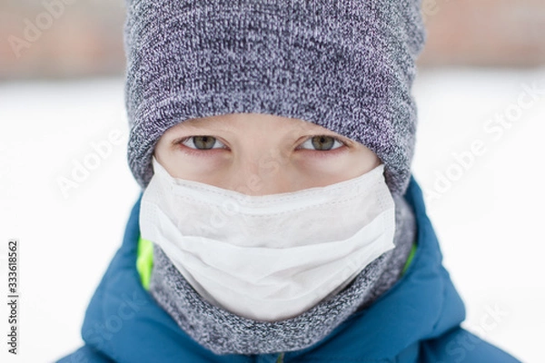 Fototapeta The danger of coronavirus. A boy on a walk walks in a medical mask on his face