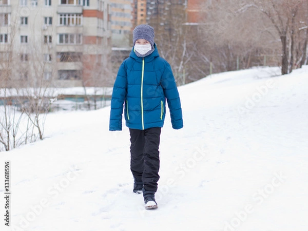 Fototapeta The danger of coronavirus. A boy on a walk walks in a medical mask on his face