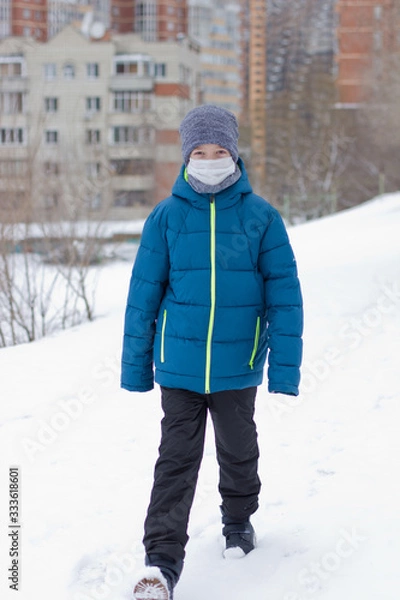 Fototapeta The danger of coronavirus. A boy on a walk walks in a medical mask on his face