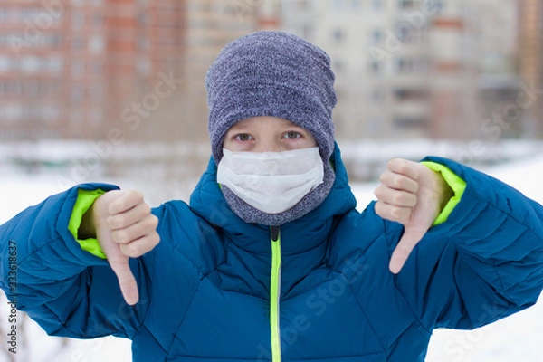 Fototapeta The danger of coronavirus. A boy on a walk walks in a medical mask on his face