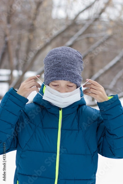 Fototapeta The danger of coronavirus. A boy on a walk walks in a medical mask on his face