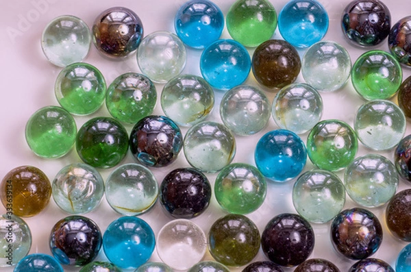 Obraz Many glass colored balls of the same size lie closely on a plane of gray color under even lighting, toned, close- up.