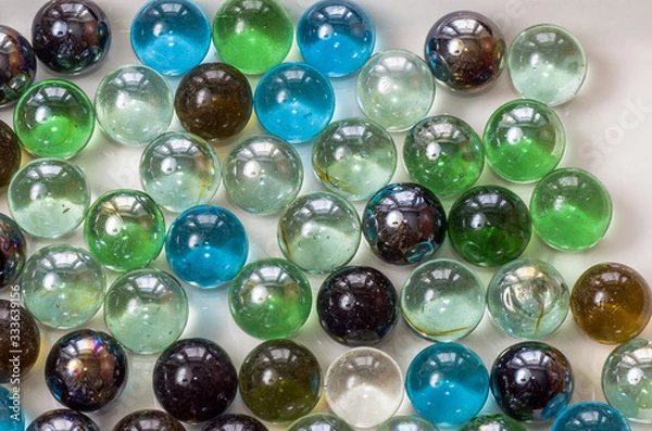 Obraz Many glass colored balls of the same size lie closely on a plane of gray color under even lighting, close- up.