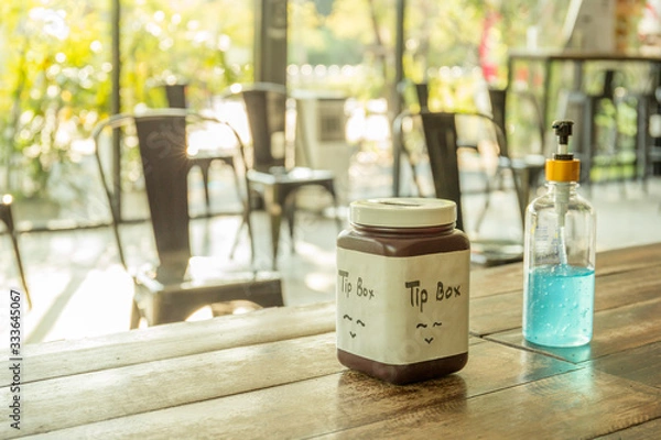 Fototapeta Social distancing, alcohol gel and tip box on table with empty chairs.