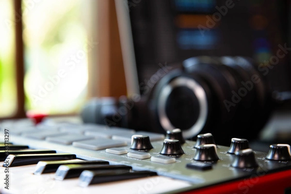 Fototapeta Midi keybard in a music producer home studio, desk with headphones and a notebook. Window with nature in the background.