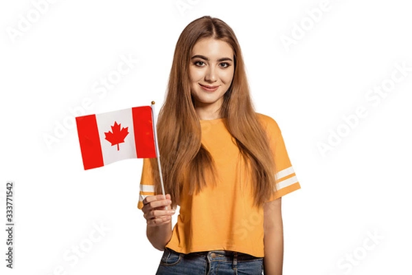 Obraz A beautiful young woman holds in her hands the flag of Canada. Exchange student, learn language. Tourist traveling. White background. Isolate. Football fan. North America.
