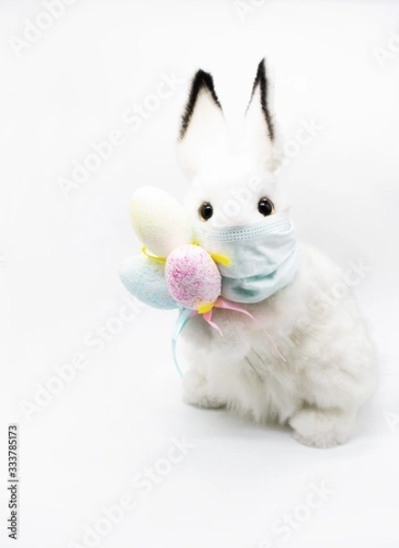 Fototapeta Easter Bunny in a facial medical mask with a bouquet of colorful eggs. The concept of Easter and quarantine during coronavirus. Like a postcard wishing you well
