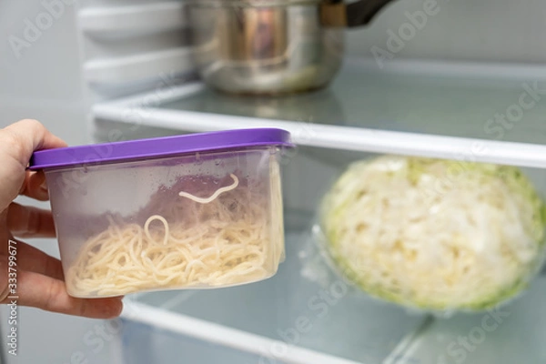 Fototapeta A hand taking plastic container with leftovers from a fridge