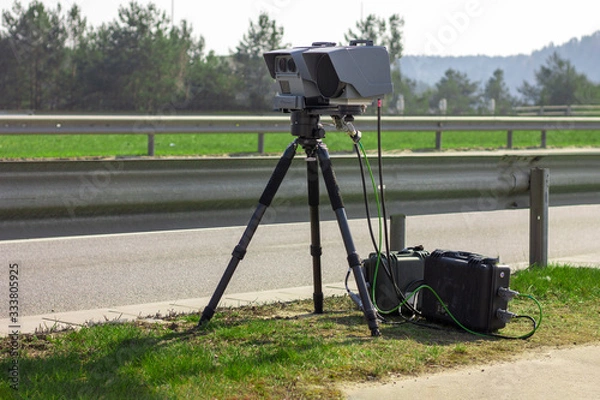 Obraz Vilnius, Lithuania - March 28, 2020: A mobile camera on a tripod standing near the road measures the speed of a passing vehicle