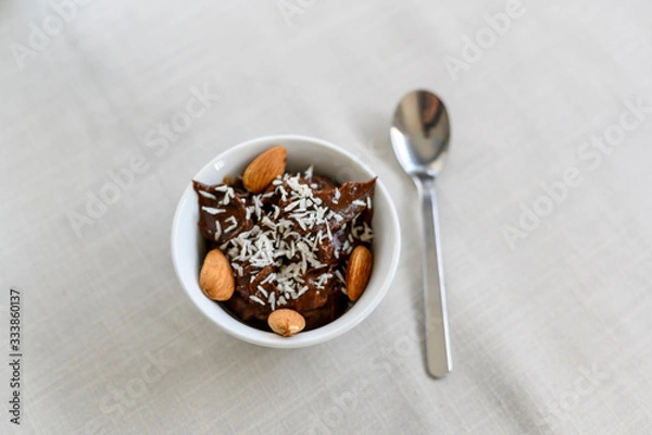 Obraz Chocolate mousse made from banana and avocado. No sugar, only natural ingredients, dates. Healthy food. Vegan. Mousse is sprinkled with coconut and garnished with almonds. Horizontal view. Copy space.
