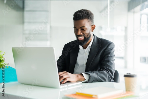 Obraz Thoughtful African American businessman using laptop, pondering project, business strategy, puzzled employee executive looking at laptop screen, reading email, making decision at office