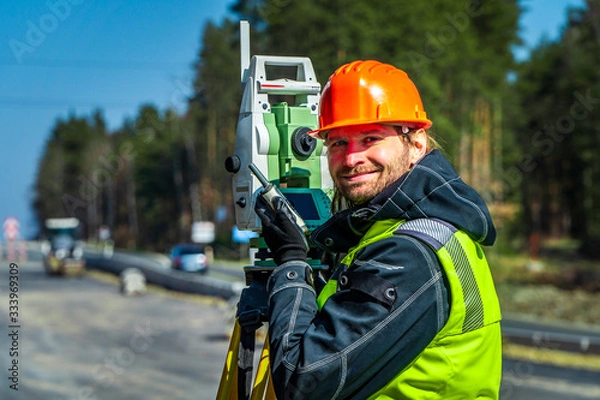 Fototapeta Surveyor engineer with equipment (theodolite or total positioning station) on the construction site of the road or building with construction machinery background