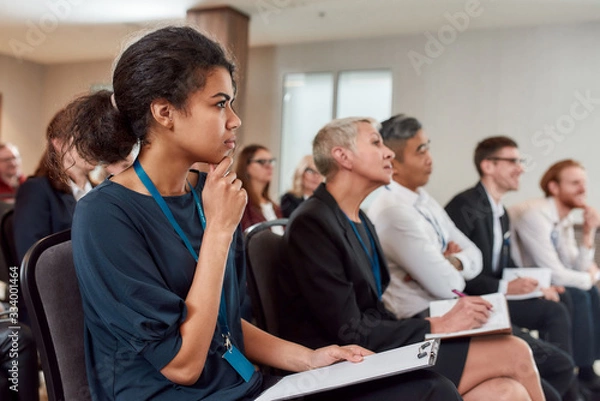 Obraz Forward-thinking. Multi-ethnic audience sitting in a row while listening to presentation at conference hall