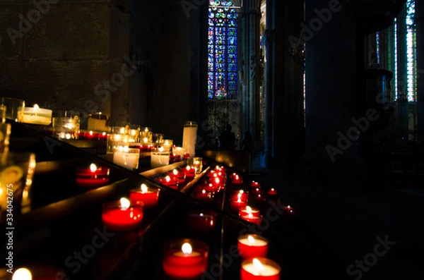 Fototapeta Flaming candles in a medieval church with stained glass windows