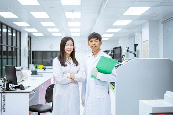 Fototapeta two young smiling scientist in white lab coat standing with automation blood analyzer at medical laboratory 