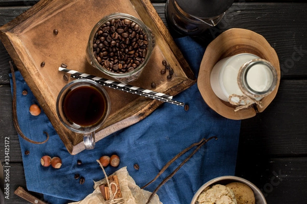 Fototapeta Cup of coffee with coffee beans, spoon, cinnamon sticks, bottle of milk and cookies on blue background