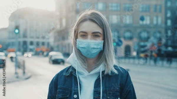 Fototapeta Young woman in medical mask standing in city street looking to camera road with cars on background Concept of health and safety life COVID-19 coronavirus virus protection pandemic in world