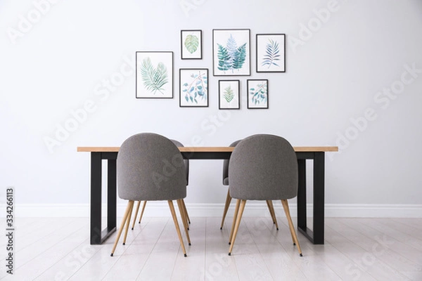 Fototapeta Stylish room interior with modern table, chairs and paintings of tropical leaves. Idea for design