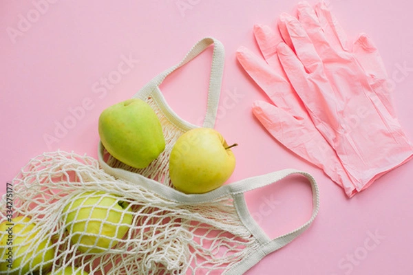 Fototapeta Safe shopping in quarantine concept. Pink gloves and tote bag with fresh apples on pink background flat lay. Stay safe. Prevention of virus epidemic. Order food online with delivery and stay home