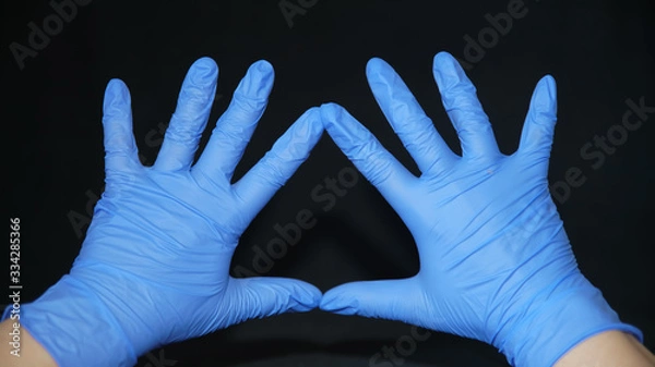 Fototapeta Hand-washing to protect against coronavirus (COVID-19) Two hands covered in blue surgical gloves, wide open, fingers apart, index fingers and thumbs forming a triangle, on a black background