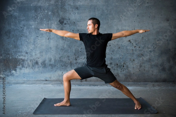 Obraz Man practicing yoga in front of a dark background. Pose is warrior II, Virabhadrasana. 