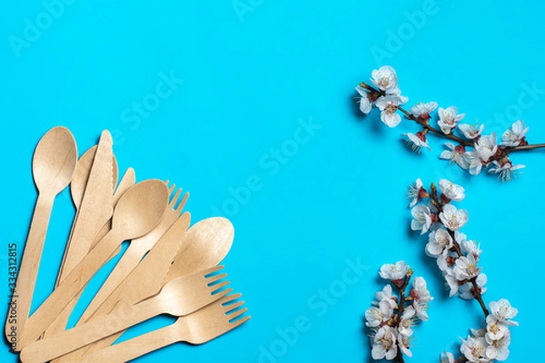 Fototapeta Disposable wooden forks and spoons are fan-shaped in the corner. blue background and several twigs of flowering trees