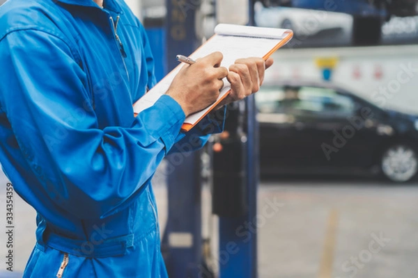 Fototapeta Auto sprawdzanie i koncepcja warsztatu samochodowego. Mechanik pisze listę kontrolną pracy do schowka w celu oszacowania wyceny naprawy dla klienta w warsztacie.