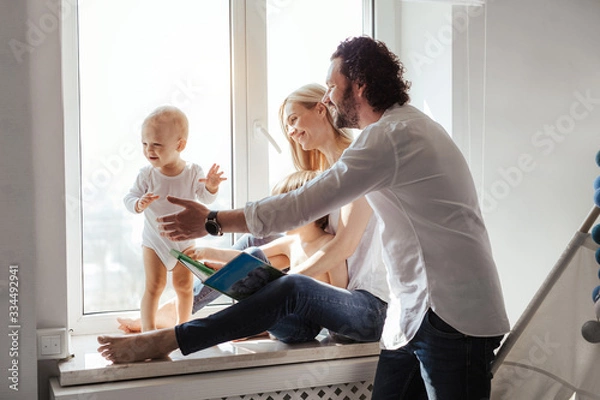 Obraz Happy smiling modern caucasian family playing and spending time in a bright white room near the window. Sunny day. Perfect parenting relationship. Parents of two cute boys.