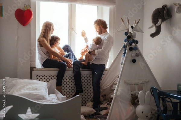 Obraz Happy smiling modern caucasian family playing and spending time in a bright white room near the window. Sunny day. Perfect parenting relationship. Parents of two cute boys.