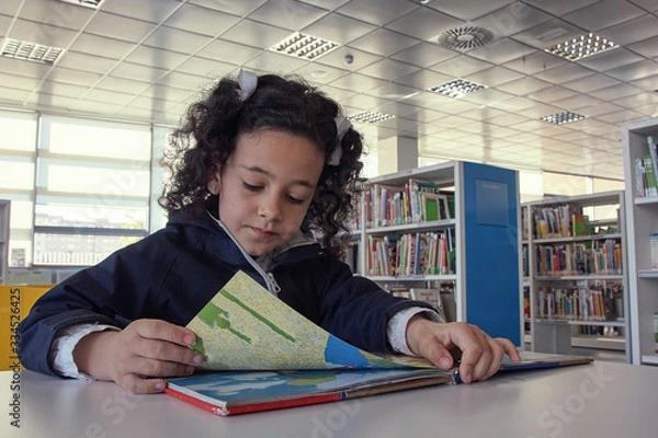 Fototapeta Niña leyendo un libro en la mesa de lectura.