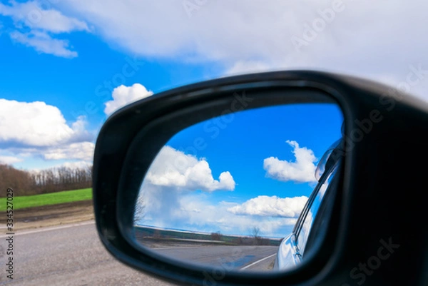 Fototapeta the blue sky with white clouds is reflected in the car mirror during the day . space for text.