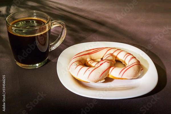 Fototapeta The pretzel cake is on a plate on the table. There is a Cup of coffee next to it. The photo of the Breakfast was taken in the morning light.