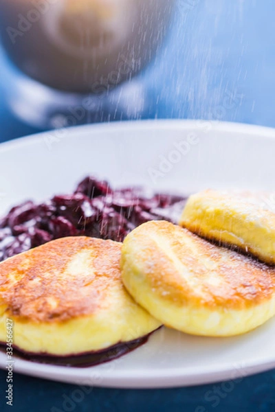 Fototapeta Breakfast and delicious concept - Pancakes from cottage cheese with jam, blue background. Sprinkle with icing sugar.