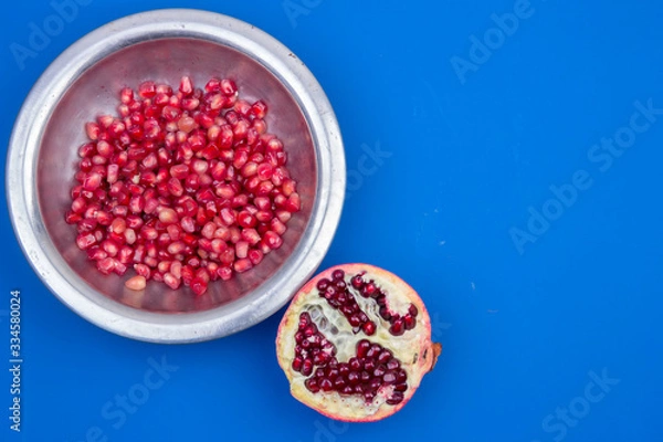 Fototapeta Pomegranate grains in a metal plate and half ripe pomegranate on a blue background