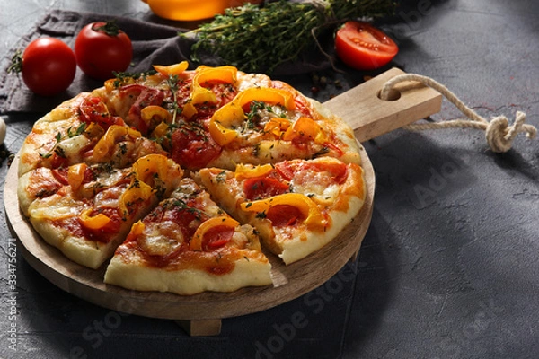 Fototapeta Italian cuisine. Pizza with mozzarella, yellow peppers, tomatoes and thyme on a wooden board on a grey background. Vegetable pizza.  Rustic. Background image, copy space