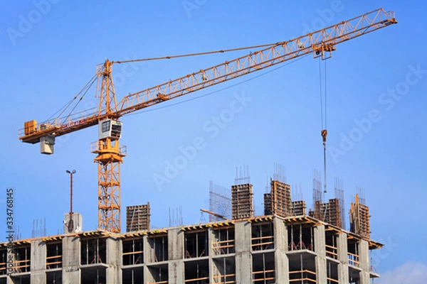 Fototapeta Single construction crane at the construction of monolithic apartment building. Building construction site with crane. The construction of multifamily modern apartment building in housing estate