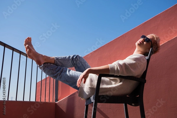 Obraz A charming woman rests on her balcony lying on a chair during a quarantine in Europe