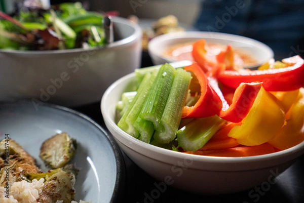 Obraz Healthy Green food such as peppers, celery, lettuce and hummus served on a dark table. Health and clean eating.