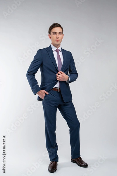 Obraz Young, handsome man in a blue suit in a white shirt with a tie on a white background in studio