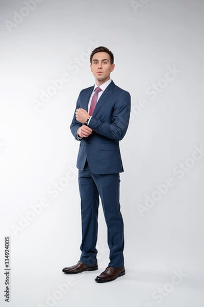 Fototapeta Young, handsome man in a blue suit in a white shirt with a tie on a white background in studio