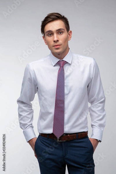 Fototapeta Young, handsome man in a white shirt with a tie on a white background in studio
