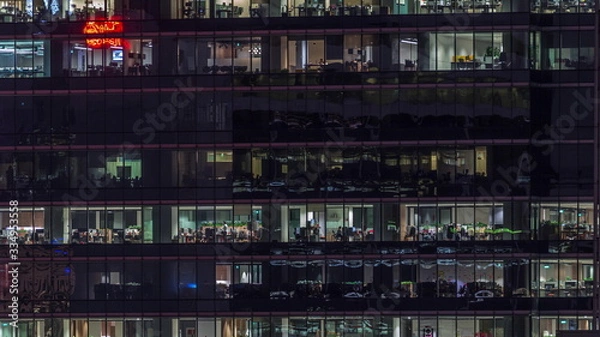 Fototapeta Modern office building with big windows at night timelapse, in windows light shines
