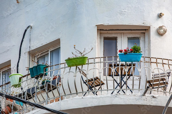 Obraz Balcony of round old-fashioned building, brown wooden table with two chairs, wrought iron fence with flower pots fixed on it, outdoor view, Tel-Aviv city