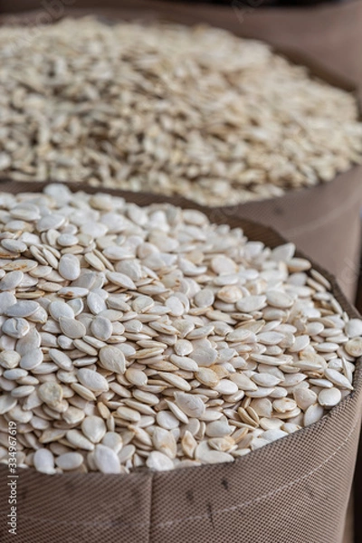 Obraz Pile of white pumpkin seeds in brown wooden bowl at food marketplace, blurred pumpkin seeds on foreground