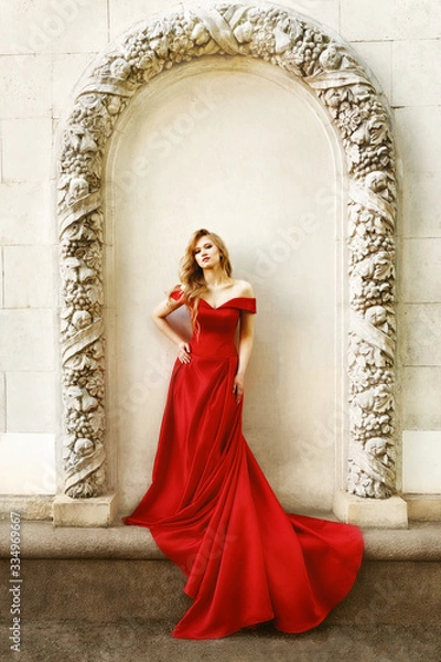 Fototapeta Beautiful blonde girl in a red long dress on a background of architecture, columns 