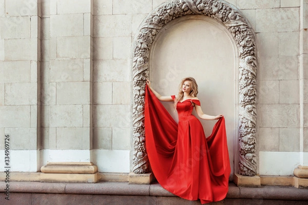 Obraz Beautiful blonde girl in a red long dress on a background of architecture, columns 